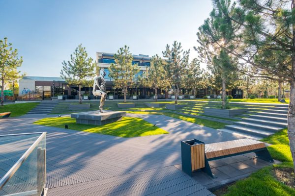 A modern urban park featuring an artistic statue, benches, and lush greenery under a bright sky.